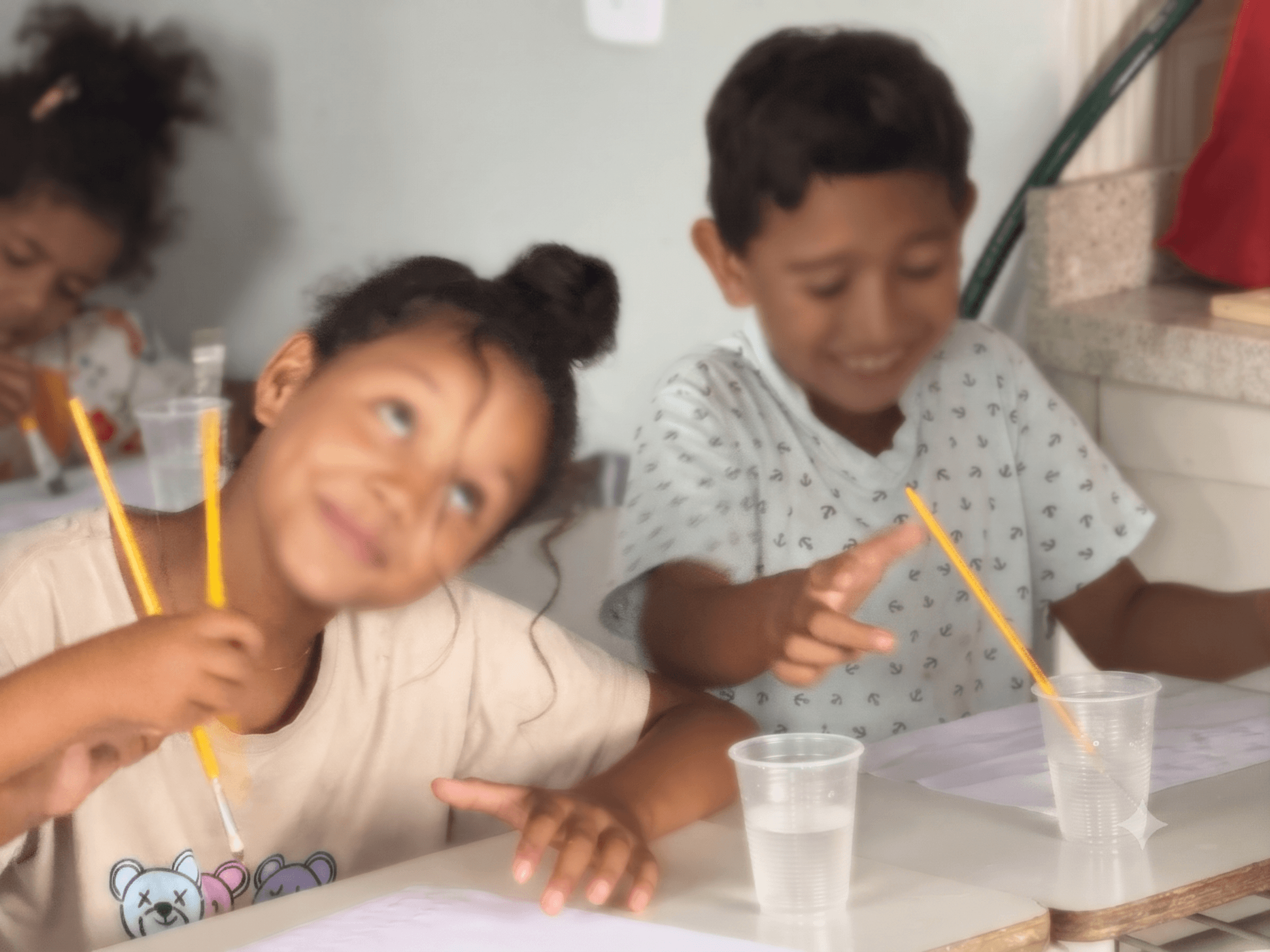 Crianças fazendo um experimento com copo, água e canudo